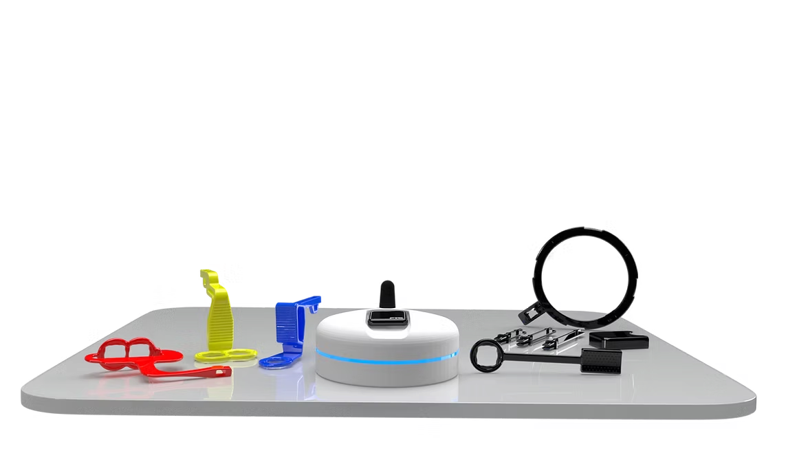 Red, yellow, and blue 3D-printed dental mouth props next to a white wireless charging dock with a blue accent ring and dental hand tools on a reflective surface